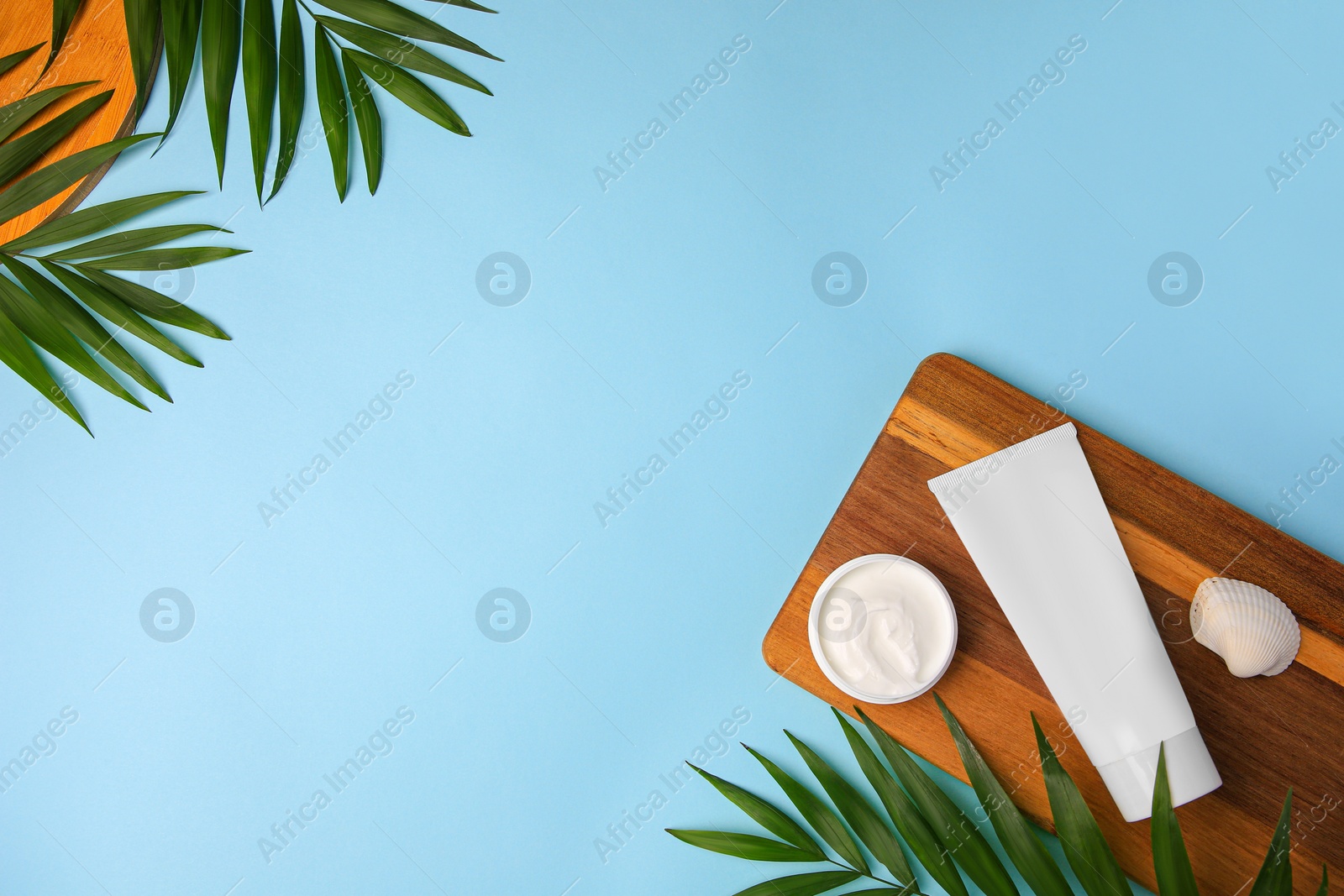 Photo of Different cosmetic products, palm leaves and shell on light blue background, flat lay. Space for text