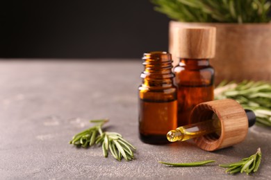 Essential oil in bottles, dropper and rosemary on grey table