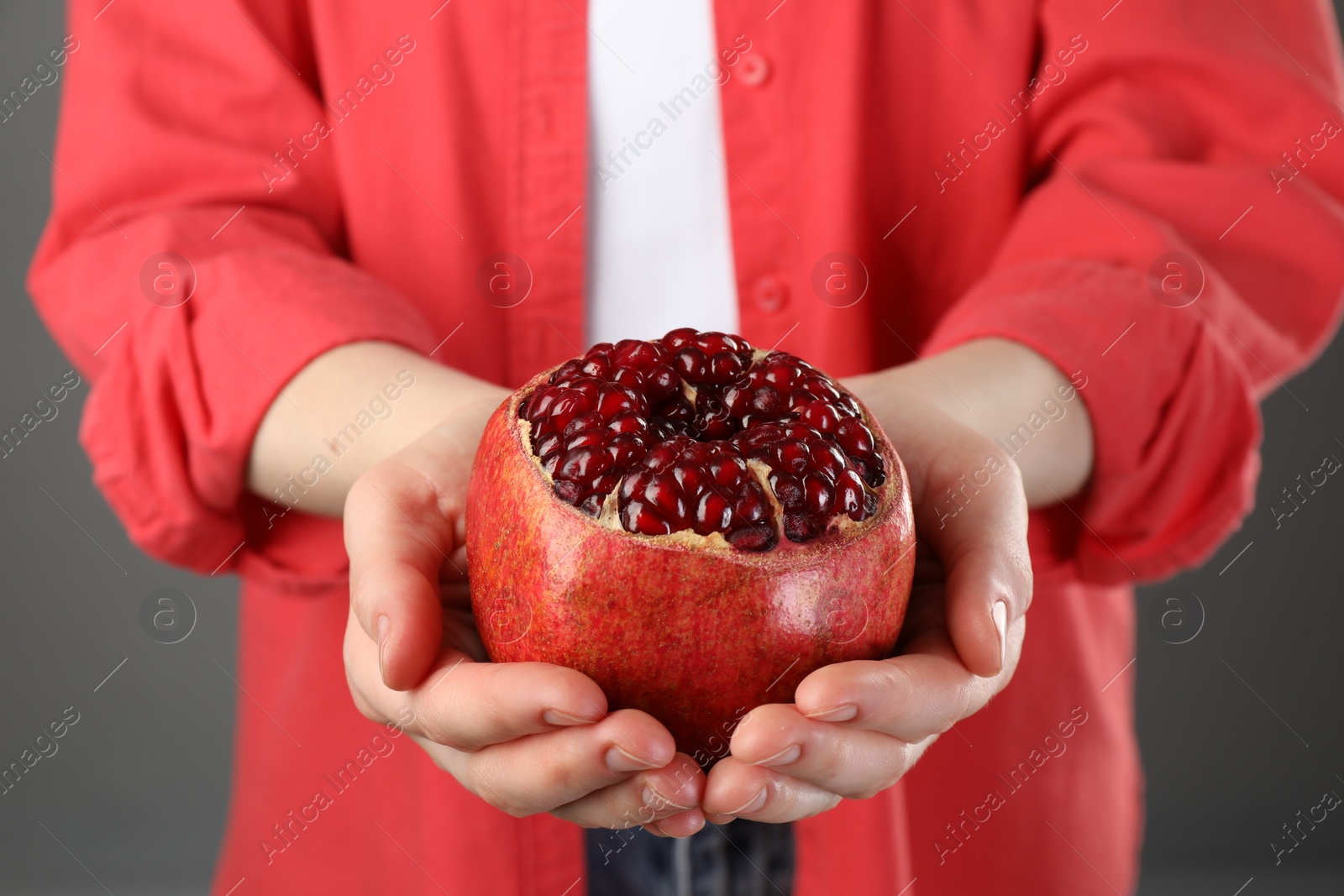 Photo of Woman holding fresh pomegranate on grey background, closeup