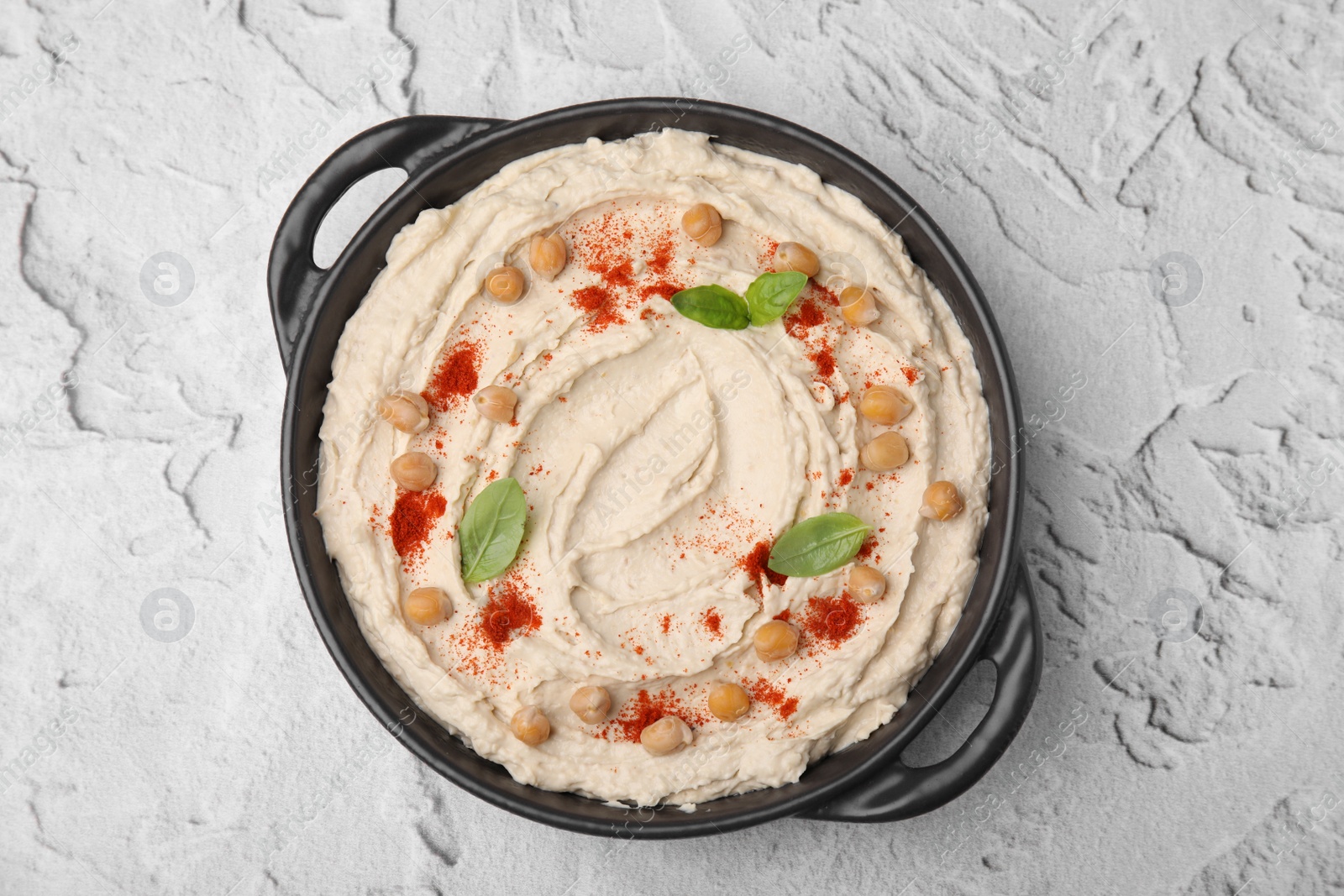 Photo of Delicious hummus with chickpeas and paprika on white textured table, top view