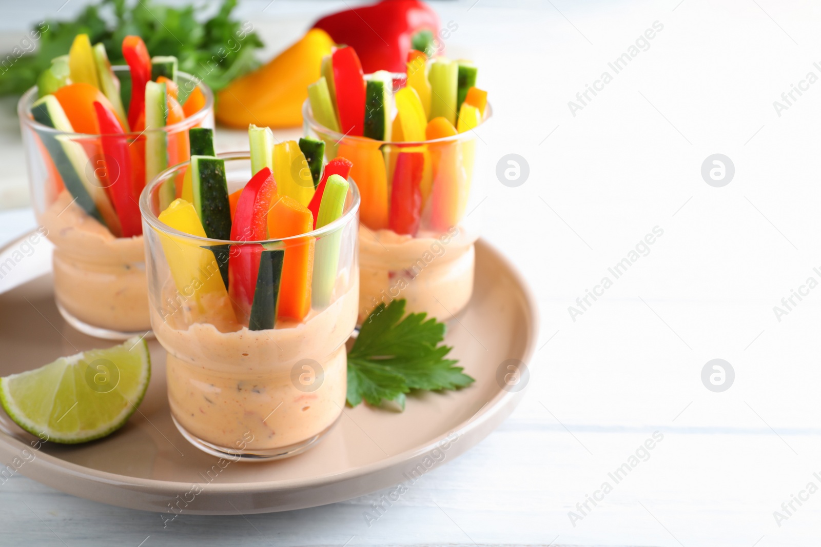 Photo of Fresh raw vegetable sticks with sauce on white wooden table. Space for text