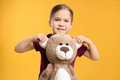 Cute girl with teddy bear on orange background