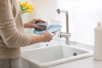 Photo of Woman washing plate above sink in modern kitchen, closeup