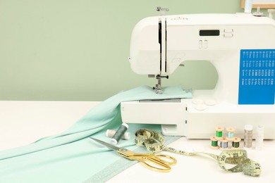 Photo of Modern sewing machine with cloth and craft accessories on white table near light green wall