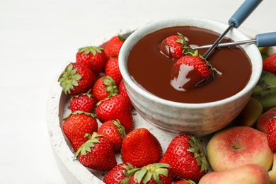 Photo of Fondue pot with chocolate and mix of fruits on white table, closeup