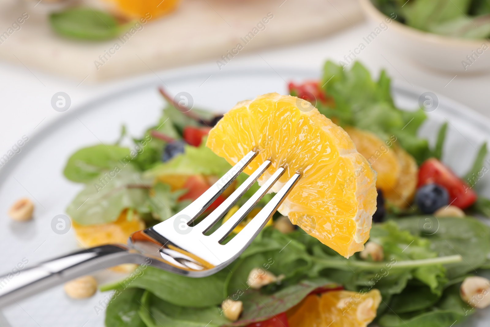 Photo of Taking piece of orange from plate with salad, closeup