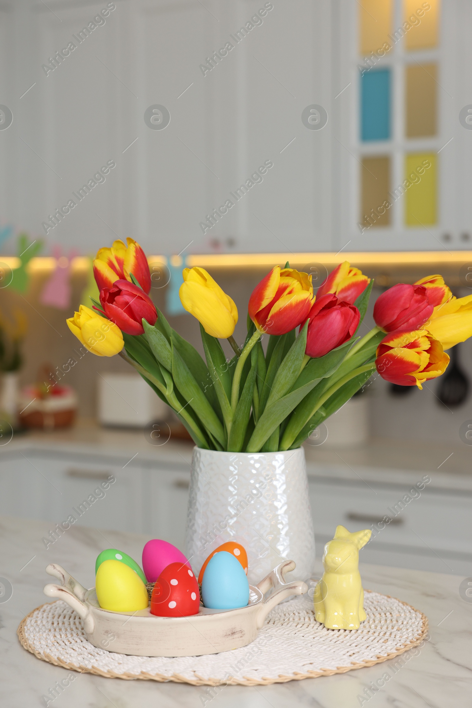 Photo of Easter decorations. Bouquet of tulips, painted eggs and bunny figure on table indoors