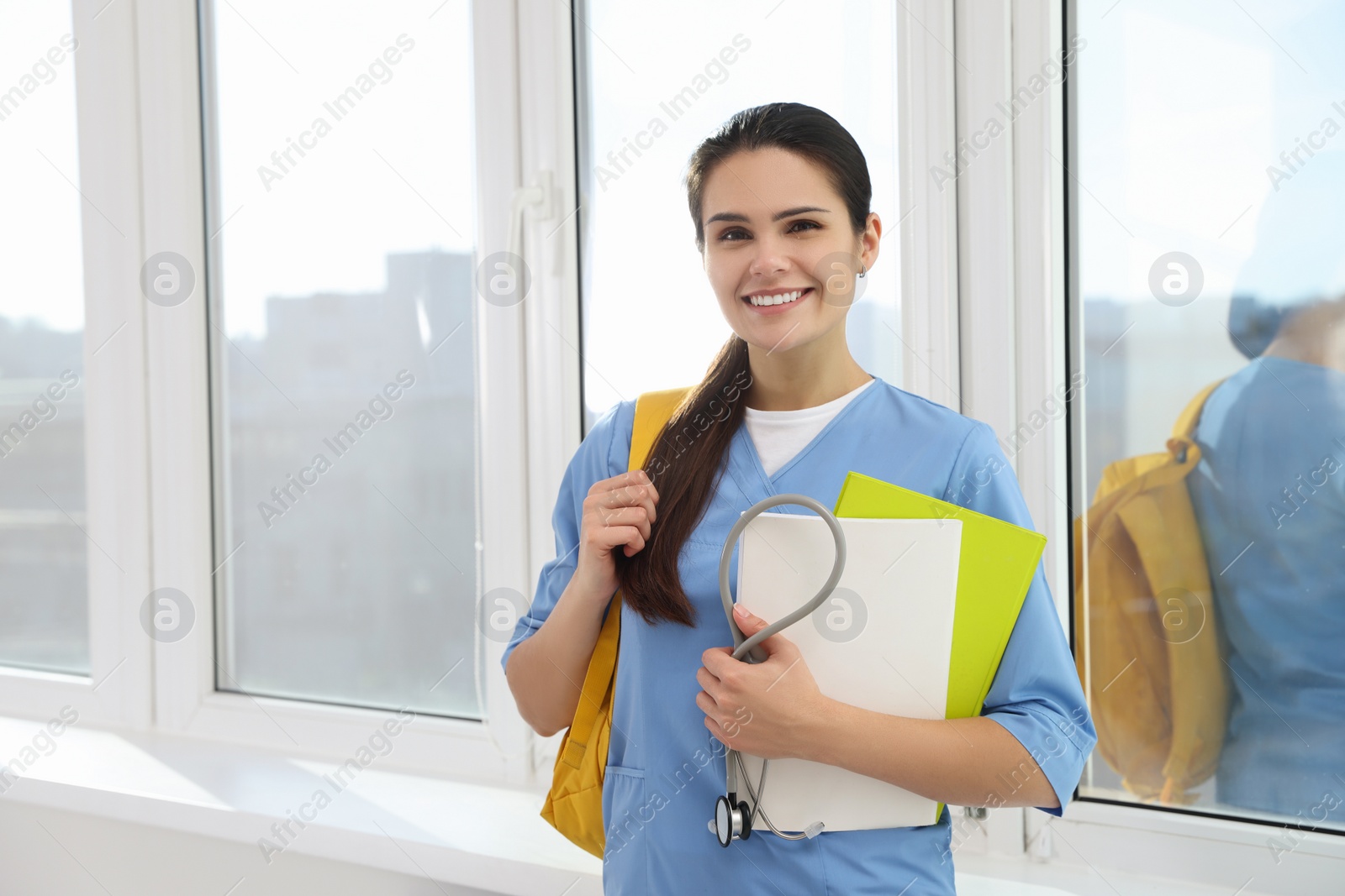Photo of Smart medical student with stethoscope and folders in college hallway, space for text