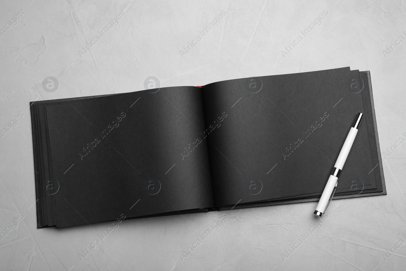 Photo of Stylish open black notebook and pen on light grey table, top view