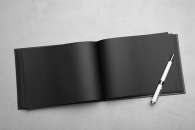 Stylish open black notebook and pen on light grey table, top view