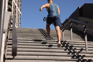 Photo of Man running up stairs outdoors on sunny day, back view