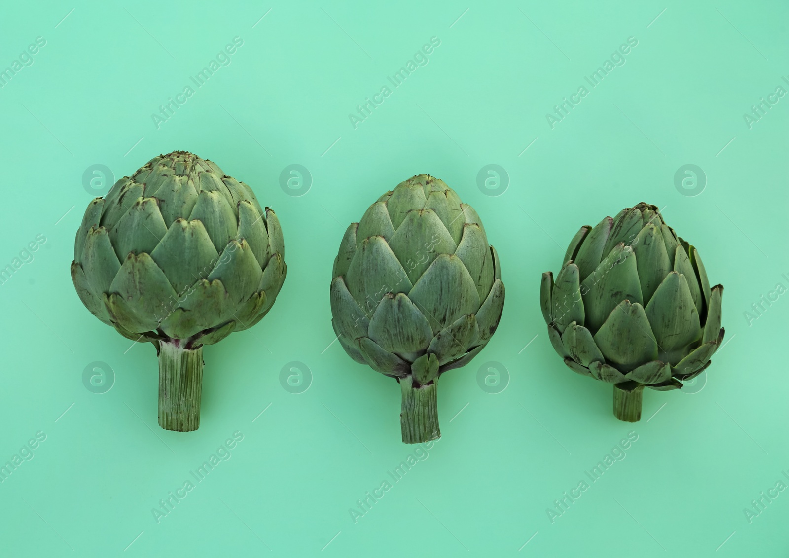 Photo of Whole fresh raw artichokes on green background, flat lay