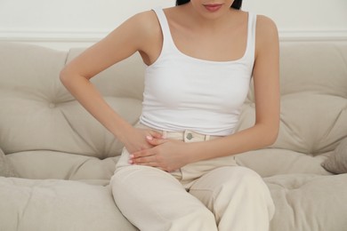 Photo of Woman suffering from appendicitis inflammation on sofa indoors, closeup