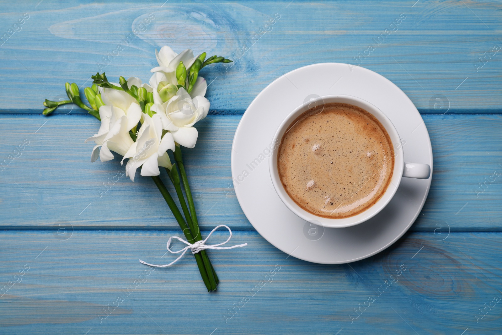 Photo of Aromatic morning coffee and flowers on light blue wooden table, flat lay