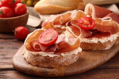 Board of tasty sandwiches with cured ham, tomato and cream cheese on wooden table, closeup