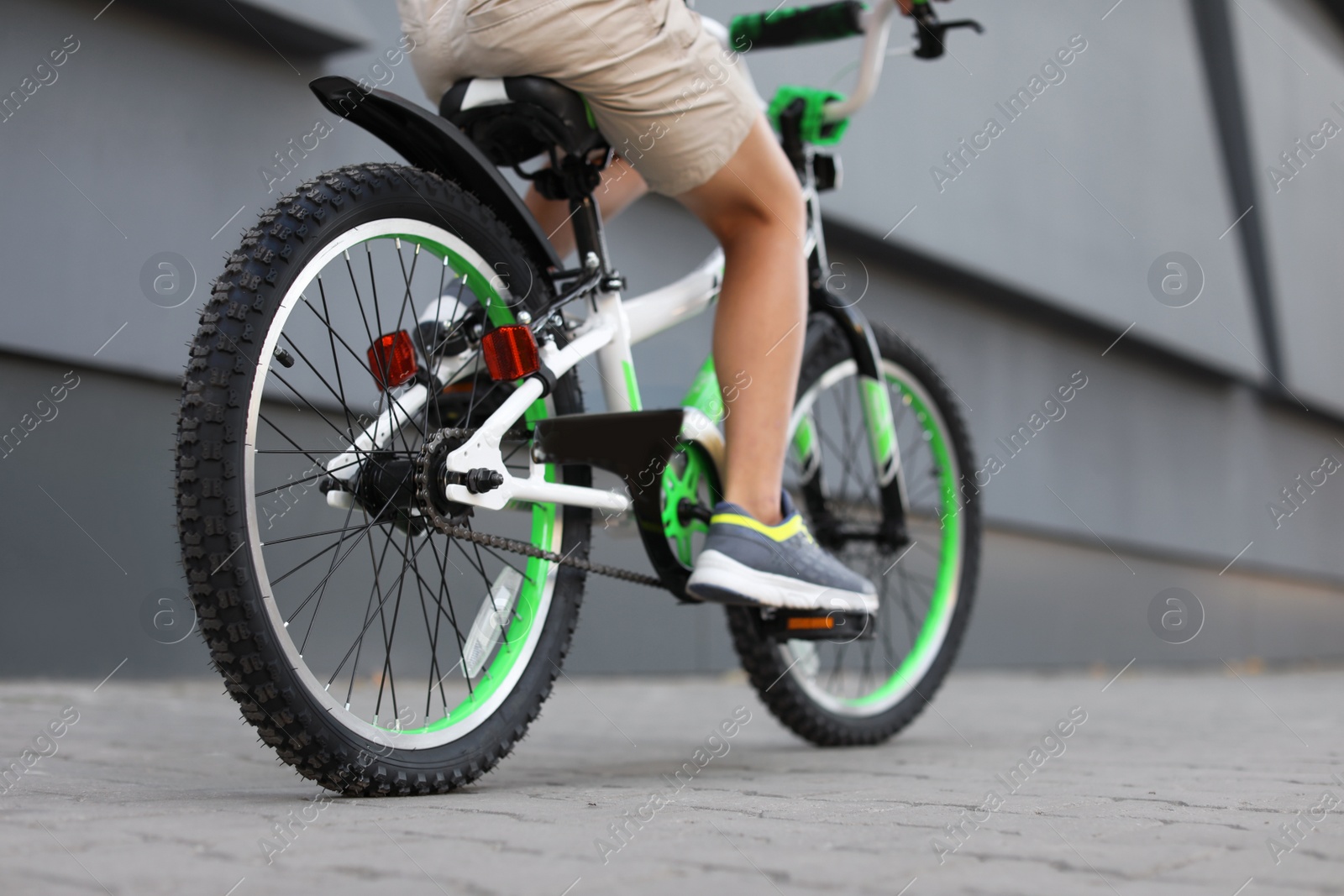 Photo of Little boy riding bicycle on street near gray wall, closeup