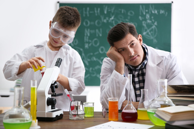 Photo of Teacher with pupil making experiment at table in chemistry class