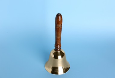 Photo of Golden school bell with wooden handle on light blue background
