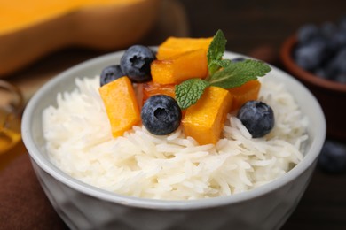 Photo of Bowl of delicious rice porridge with blueberries and pumpkin on table, closeup