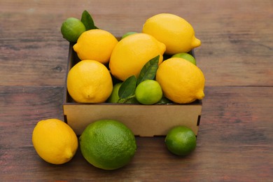 Photo of Many fresh lemons and limes with leaves on wooden table