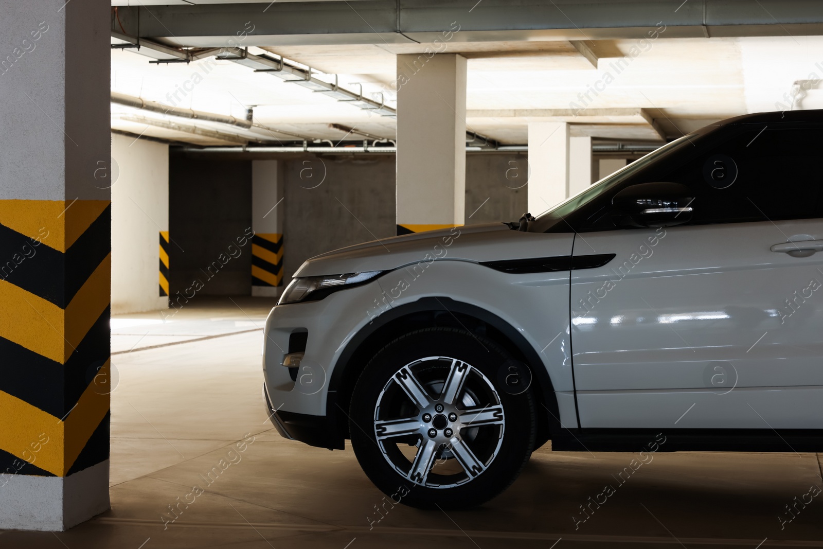 Photo of White car near column with warning stripes in parking garage