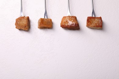 Photo of Fondue forks with pieces of fried meat on white textured table, flat lay. Space for text