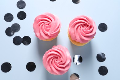 Photo of Delicious cupcakes with bright cream and confetti on light background, flat lay