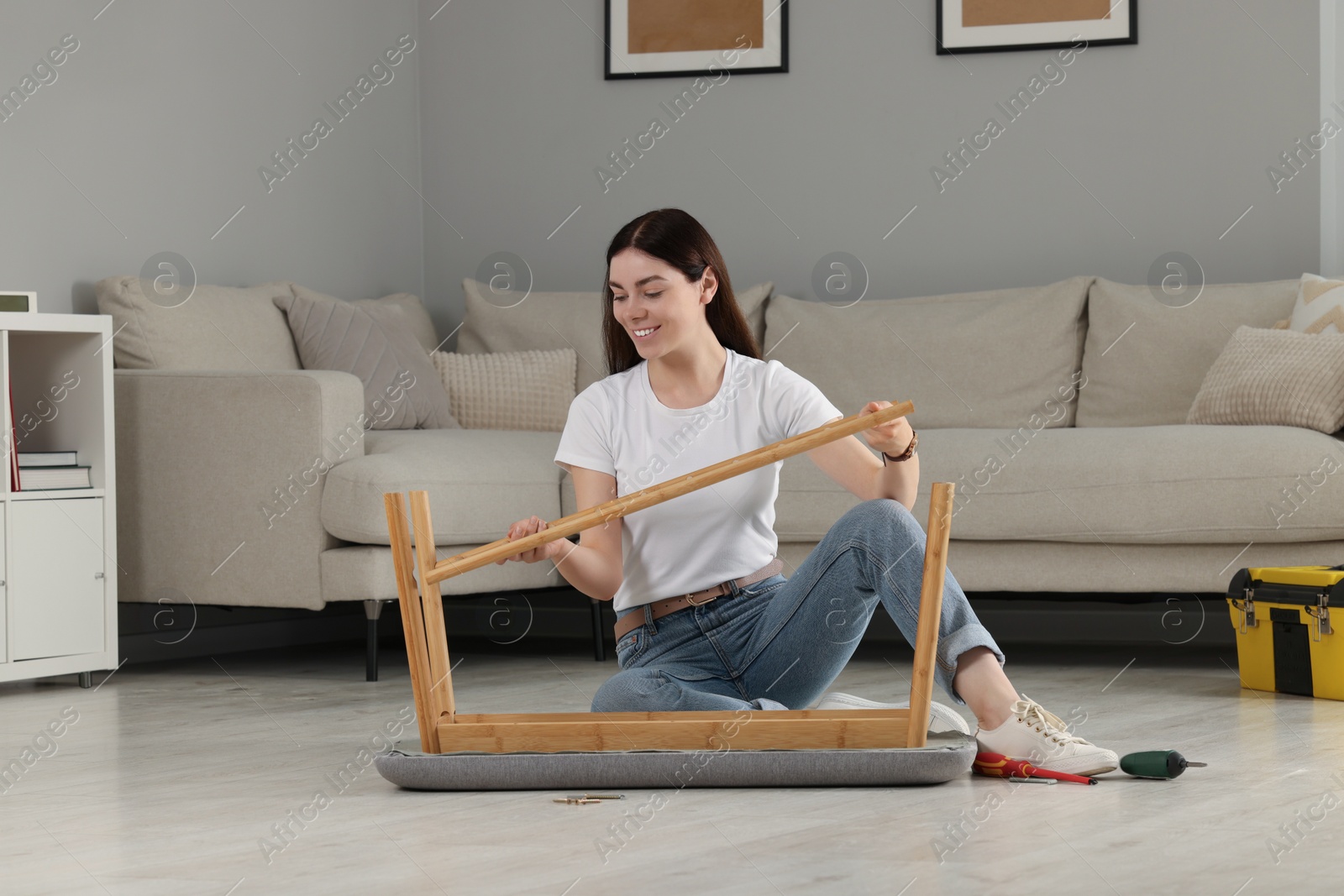 Photo of Young woman assembling shoe storage bench on floor at home