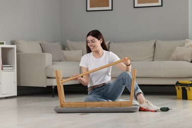 Photo of Young woman assembling shoe storage bench on floor at home