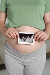 Photo of Pregnant woman with ultrasound picture of baby in room, closeup