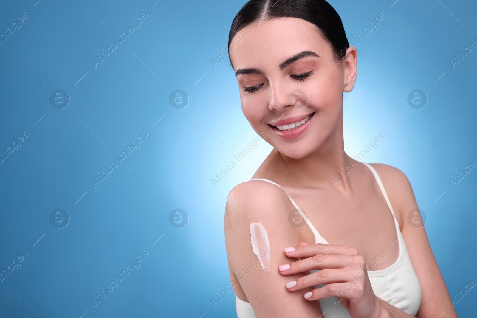 Photo of Beautiful woman with smear of body cream on her shoulder against light blue background, space for text