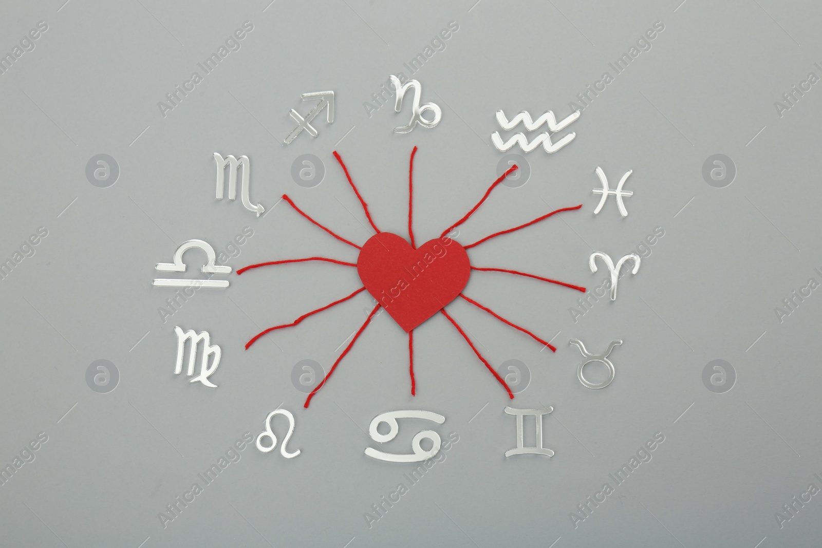 Photo of Zodiac compatibility. Signs, red heart and threads on grey background, flat lay