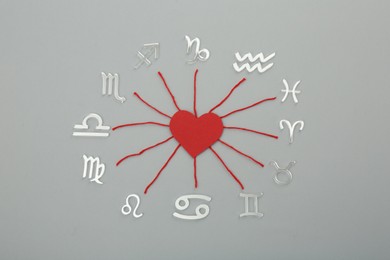 Zodiac compatibility. Signs, red heart and threads on grey background, flat lay