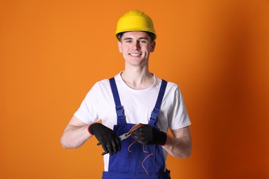 Photo of Young man holding pliers and wires on orange background