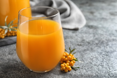 Photo of Delicious sea buckthorn juice and fresh berries on grey table, closeup. Space for text