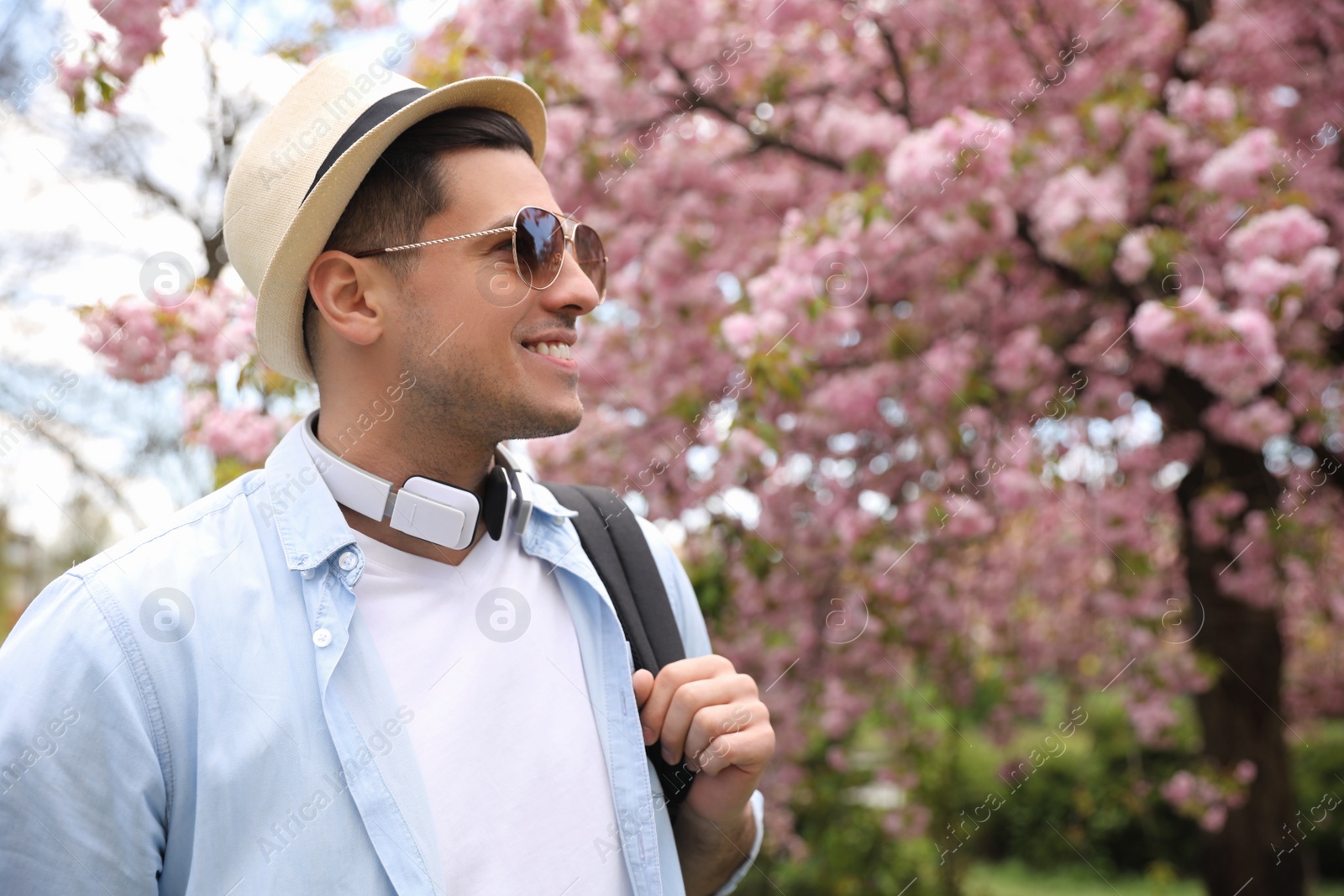 Photo of Happy male tourist with headphones in blossoming park on spring day