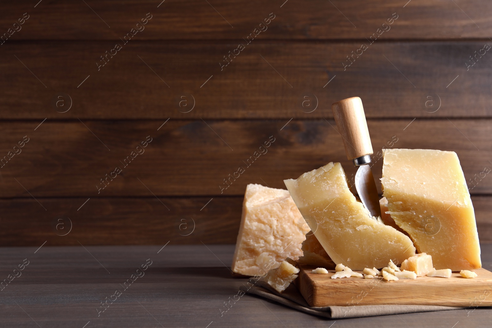 Photo of Parmesan cheese with wooden board and knife on table. Space for text