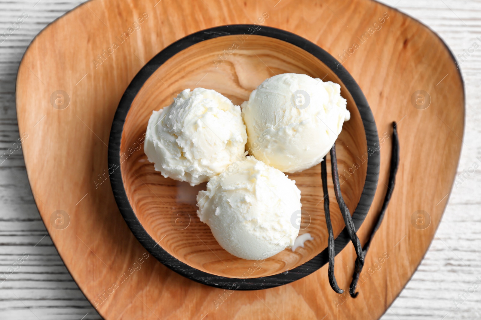 Photo of Plate with tasty vanilla ice cream on wooden background, top view