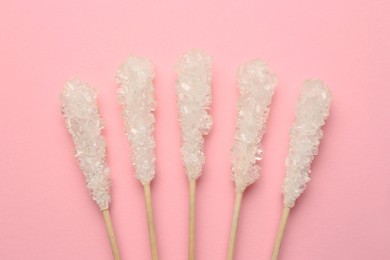 Photo of Wooden sticks with sugar crystals on pink background, flat lay. Tasty rock candies