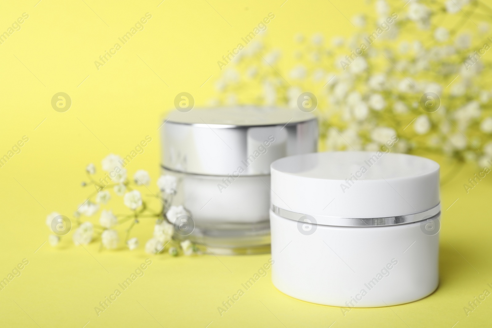 Photo of Luxury face creams and flowers on yellow background