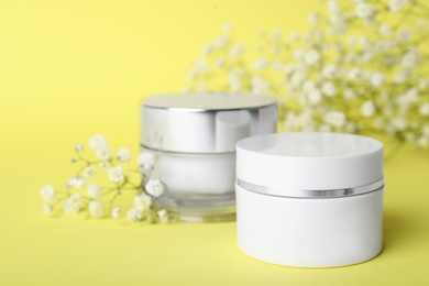 Luxury face creams and flowers on yellow background