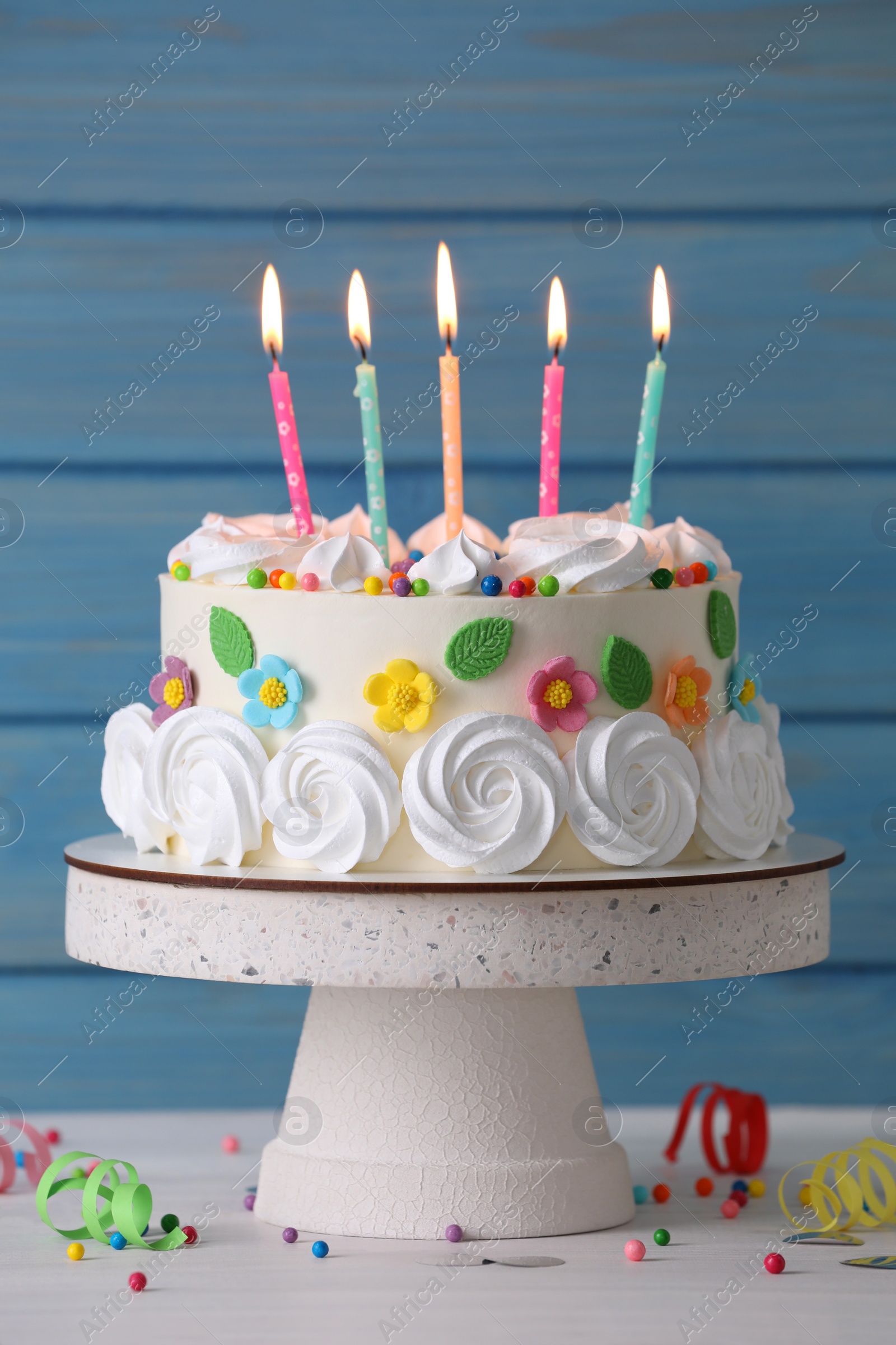 Photo of Delicious birthday cake and party decor on white wooden table against light blue background