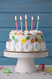 Photo of Delicious birthday cake and party decor on white wooden table against light blue background