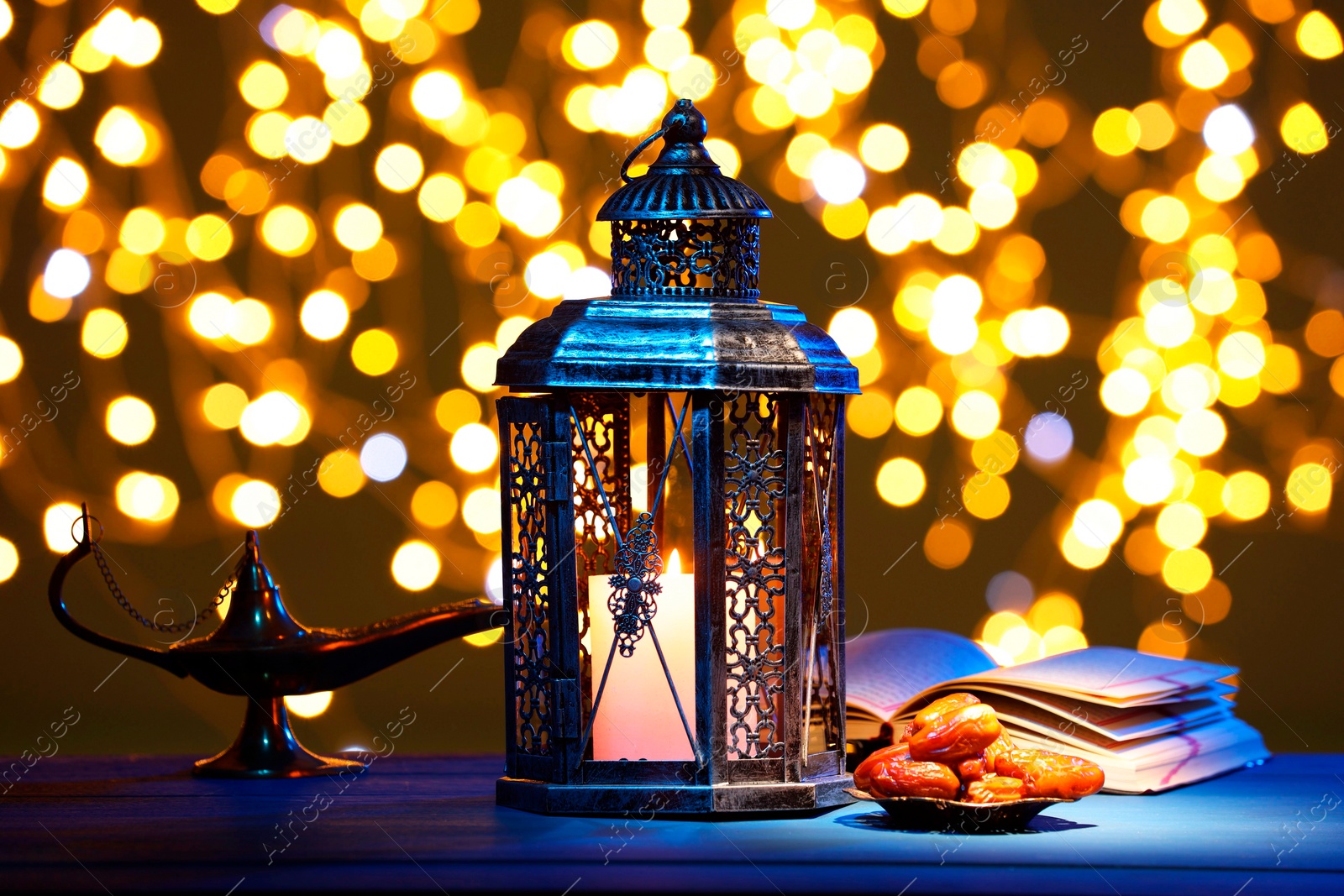 Photo of Arabic lantern, Quran, dates and Aladdin magic lamp on table against blurred lights at night