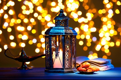 Arabic lantern, Quran, dates and Aladdin magic lamp on table against blurred lights at night