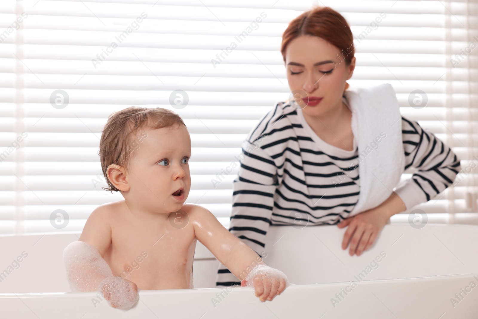 Photo of Mother washing her little baby in tub at home, selective focus