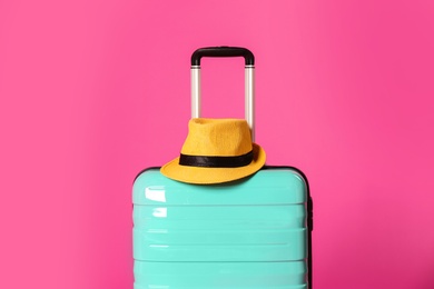 Stylish suitcase with hat on color background