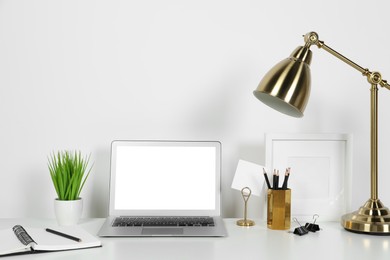 Photo of Cozy workspace with laptop, lamp and stationery on white desk at home