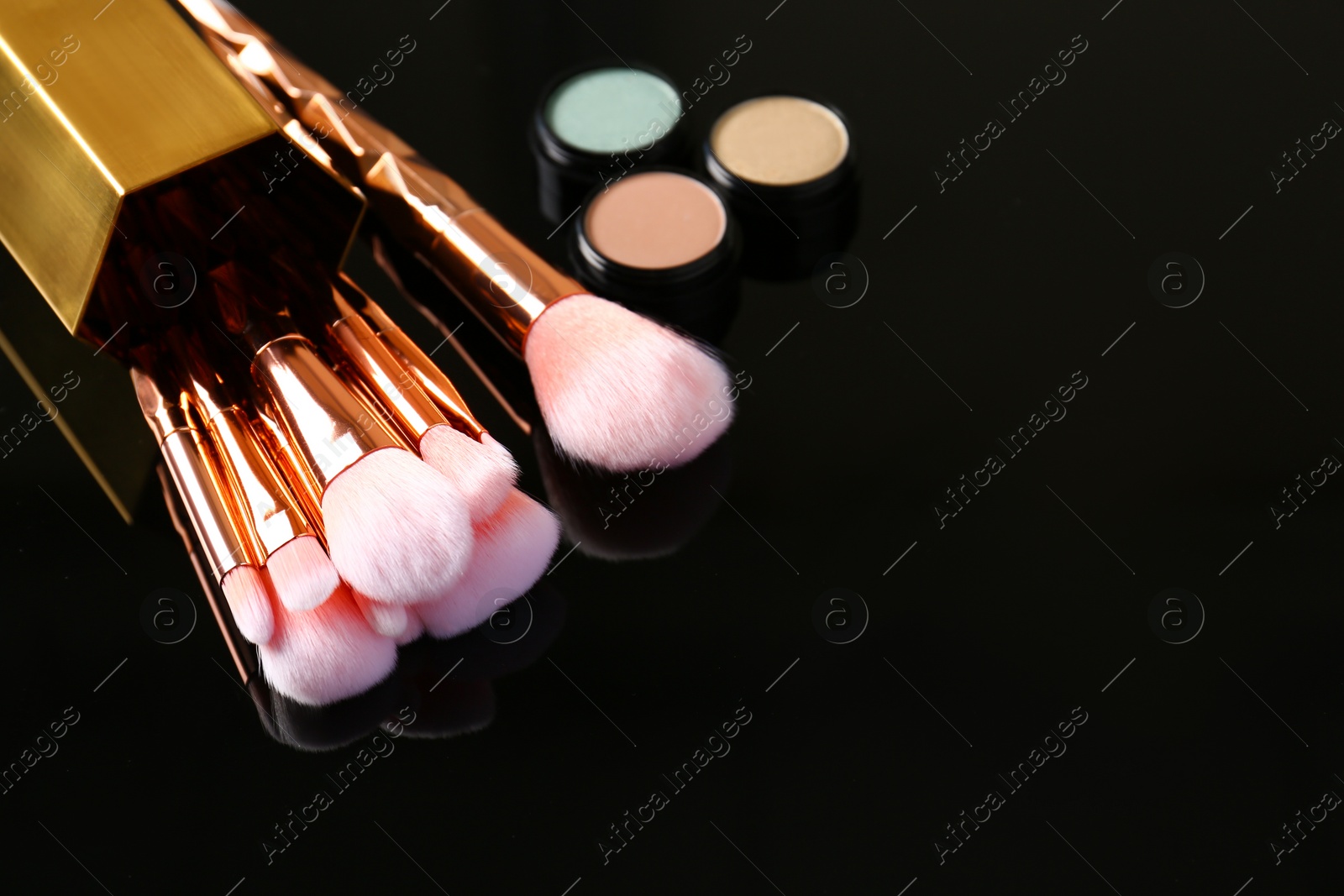 Photo of Set of makeup brushes and cosmetic on dark background, space for text