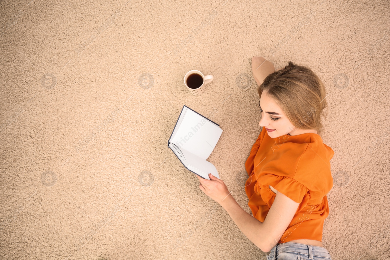 Photo of Young woman with book and coffee lying on floor at home, top view